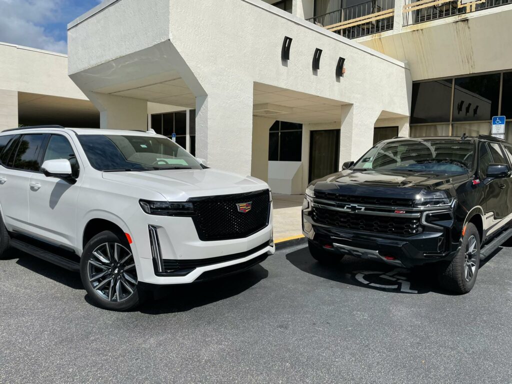 Two modern SUVs are parked side by side outside a building, ready for an airport transfer.
