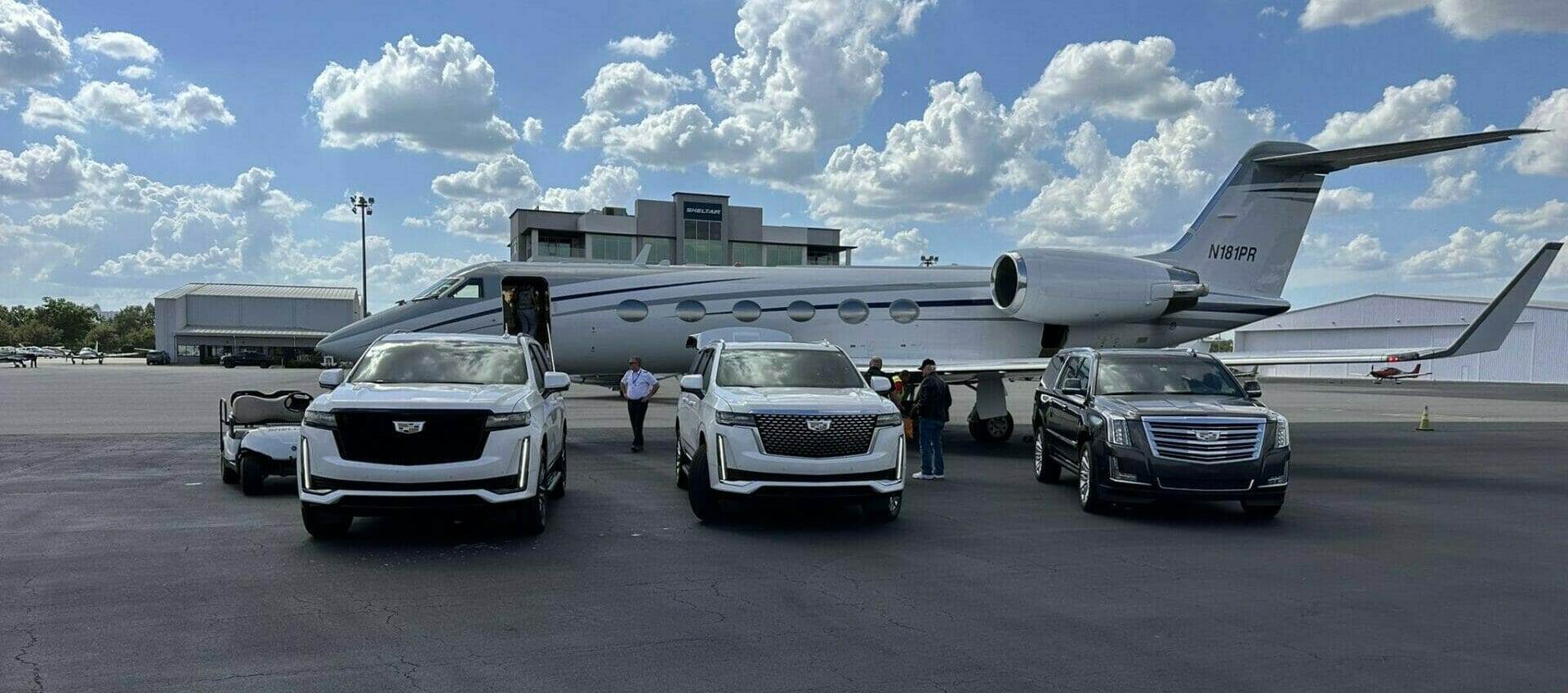Private jet parked on tarmac with two luxury limousines and several individuals standing nearby.