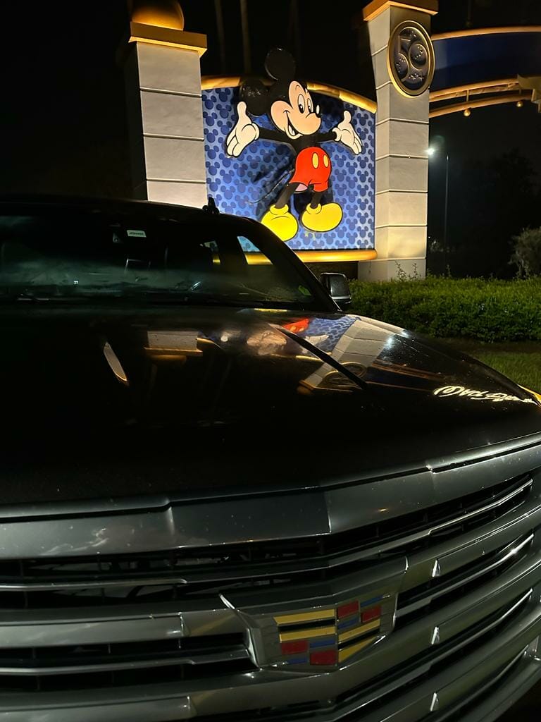A parked car in the foreground with a depiction of a classic animated character on a wall at Orlando, lit up at night.