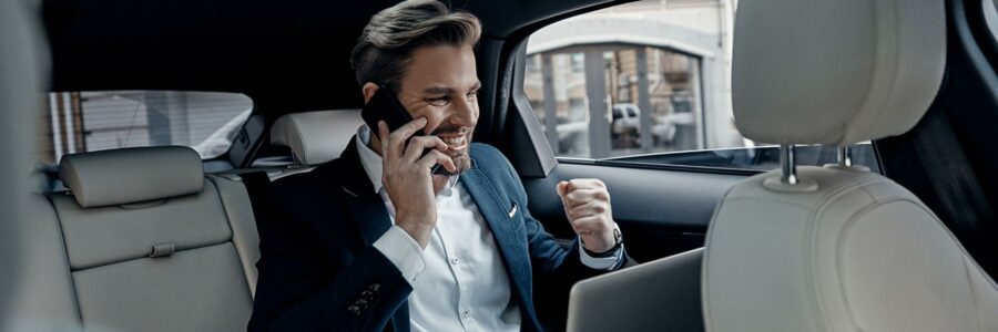 Businessman celebrating success while talking on the phone in the backseat of a limousine.