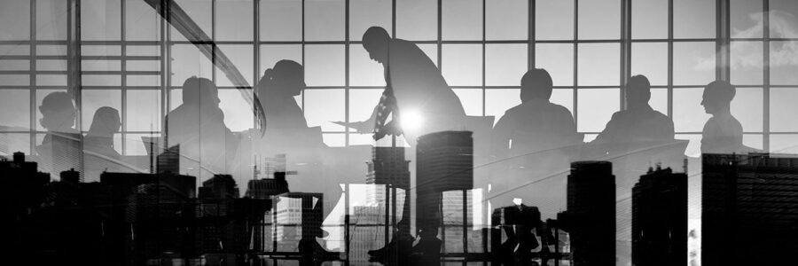 Silhouettes of business professionals in a meeting behind glass panels with cityscape and airport transfer reflections.