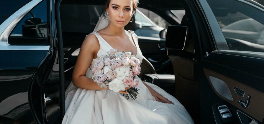 A bride in a white dress holding a bouquet while sitting in a car for her Disney parks transfer in Orlando.